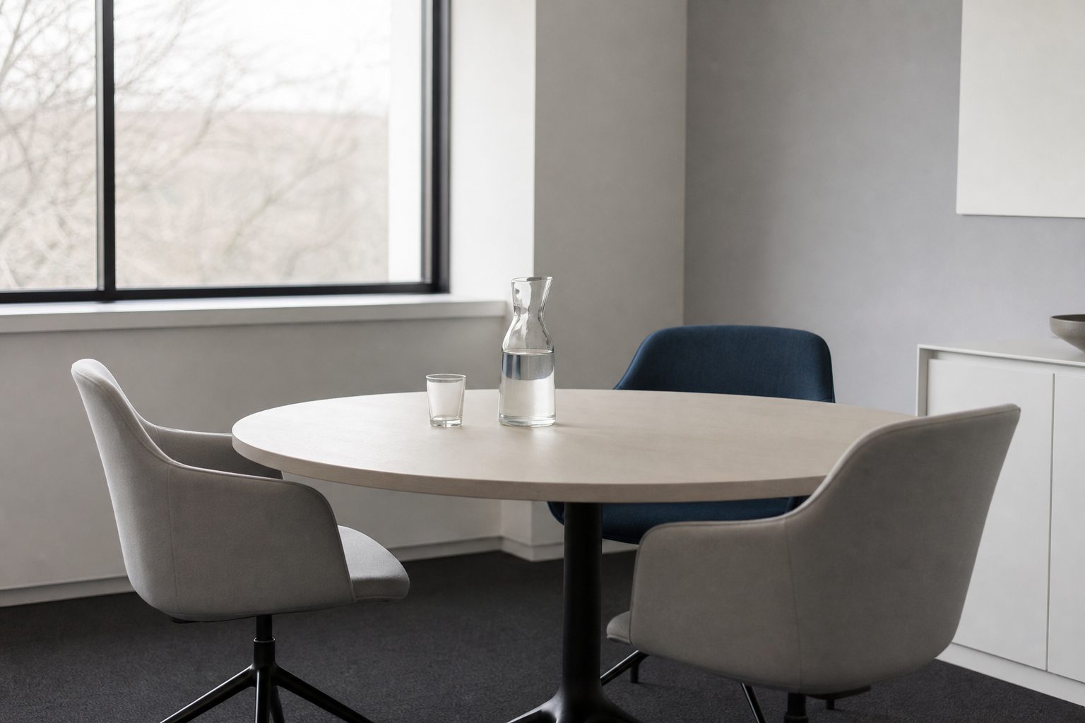 Quiet mediation room with a round pale table, empty chairs and a water carafe